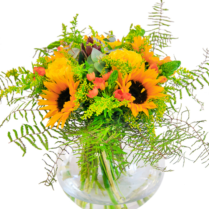 At first glance, this sumptuous bouquet sparkles with sun-kissed exuberance-layers of sunflower petals and gold-toned roses interlace, each bloom unfurling as if soaking up the light of a warm Whitechapel afternoon. Between the stars of the bouquet, deep green leaves and wispy vines arch gracefully, reminiscent of garden paths winding through the historic East End. Scarlet hypericum berries, glossy and plump, nestle among the petals, providing playful contrast and mimicking the pops of color found in the flower stalls near Whitechapel Gallery. The rounded glass vase, clear and simple, lets every stem and detail of the bouquet's architecture shine, its clarity evoking the transparency and welcoming vibe of the local neighbourhood. Up close, the tactile wonders are endless-velvety sunflowers, tightly whorled rose petals, the crisp snap of verdant greens. Subtle scents rise from the arrangement, a mix of fresh-cut flowers and a hint of eucalyptus, calling to mind the open-air energy of Whitechapel's bustling weekends. This arrangement is a heartfelt choice for birthdays, anniversaries, or any occasion where light and happiness are meant to be at the center, curated with the skill and community touch of a local Whitechapel florist.